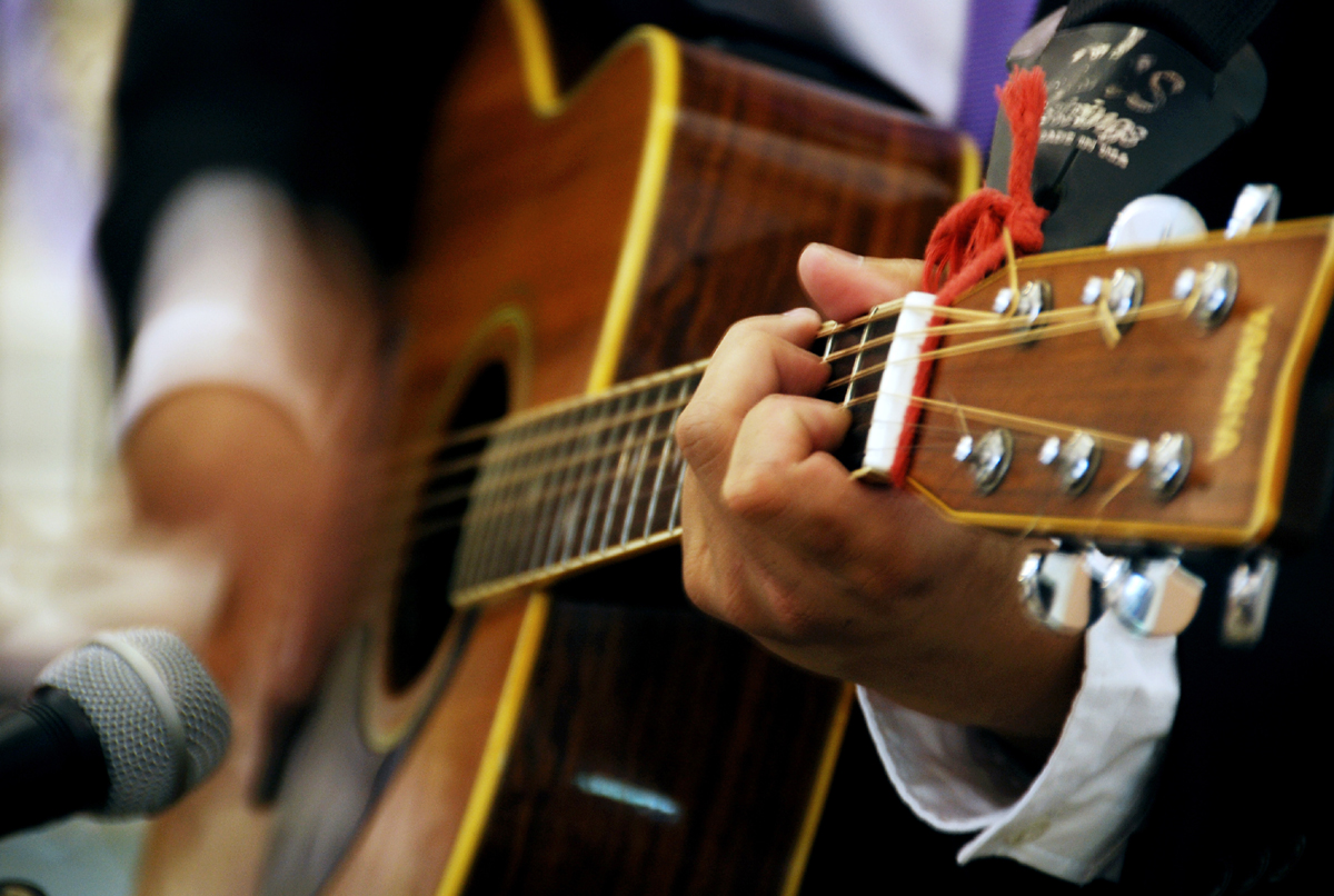 En person spelar på en akustisk gitarr. Bilden är beskuren så att bara gitarren och händerna syns.