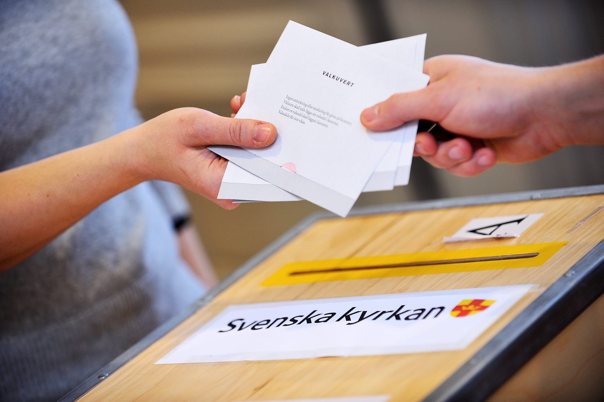 Händer som räcker över valkuvert i samband med kyrkoval. 