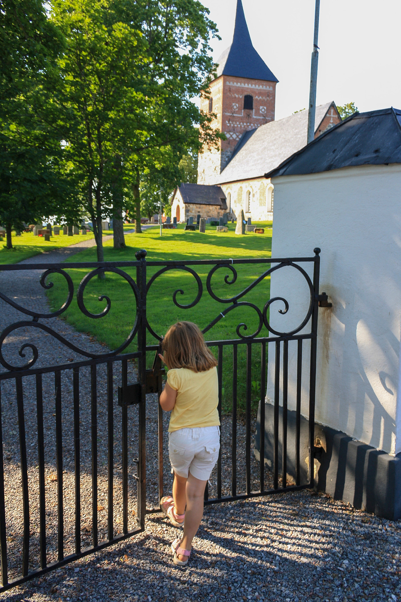 Flicka står vid svarta järngrindar. På andra sidan grinden fortsätter en grusgång upp till en stenkyrka.