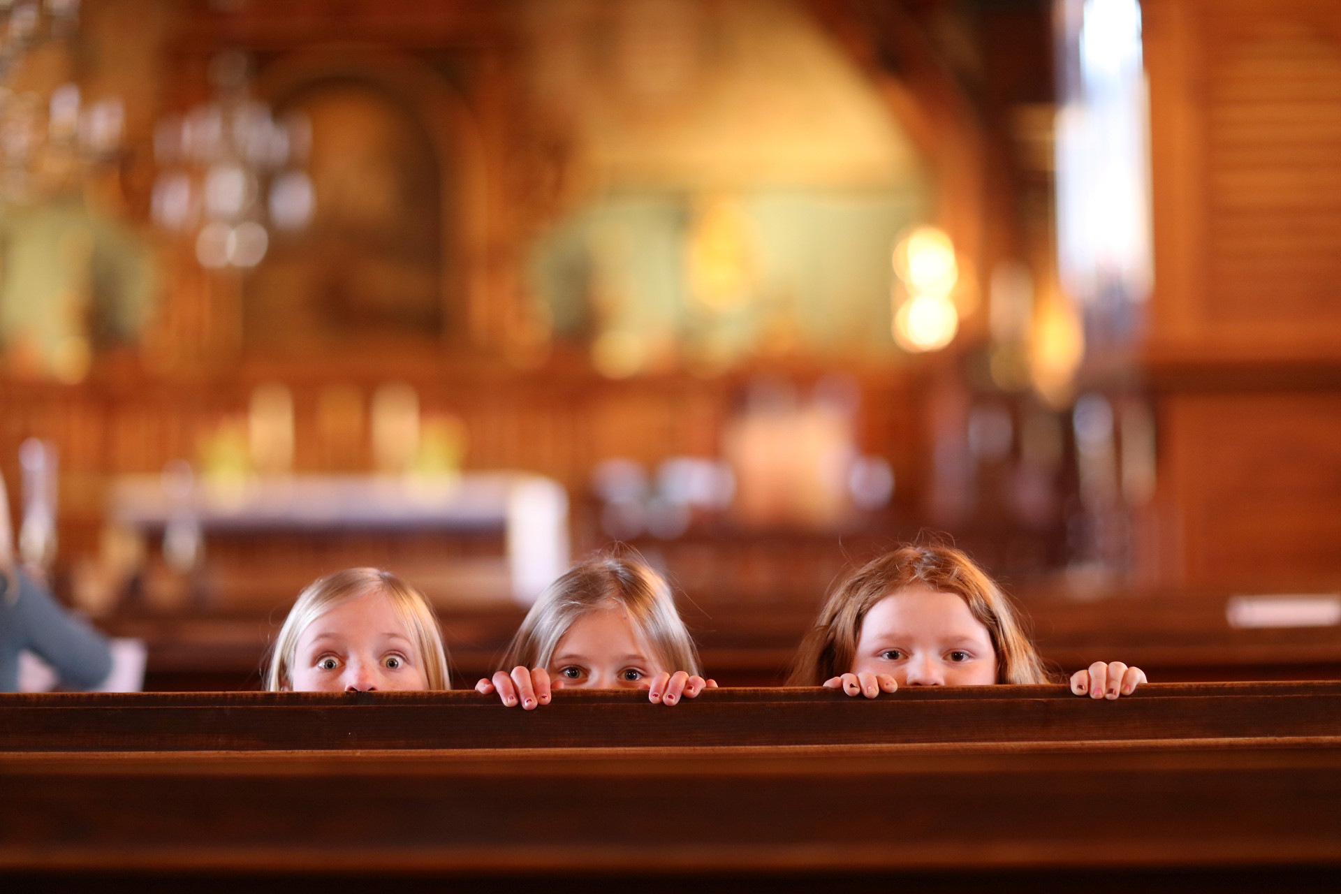 Barn som tittar fram bakom kyrkbänk.