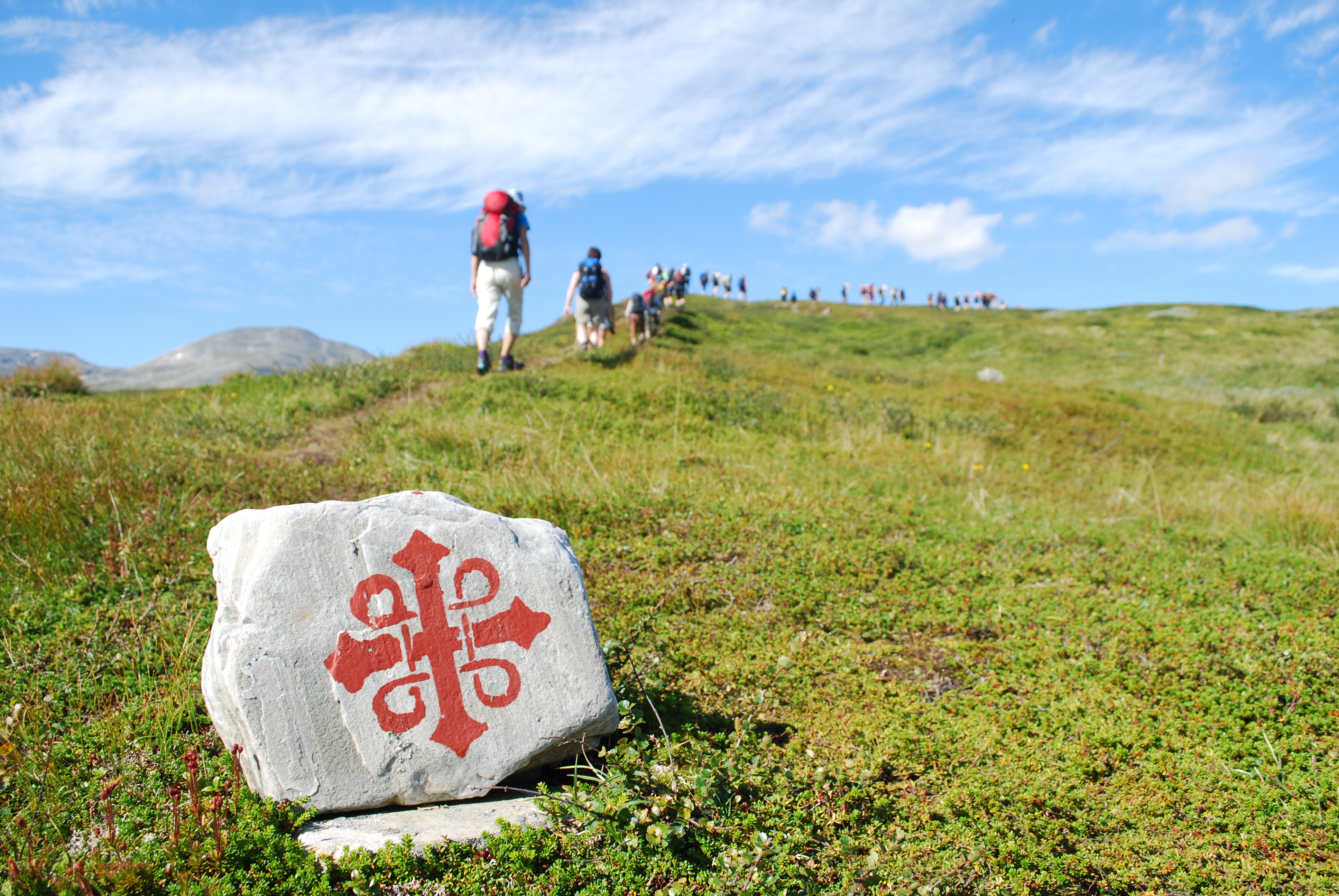 Rombosymbol målad på en sten. Pilgrimsvandrare går bortåt i bakrunden.