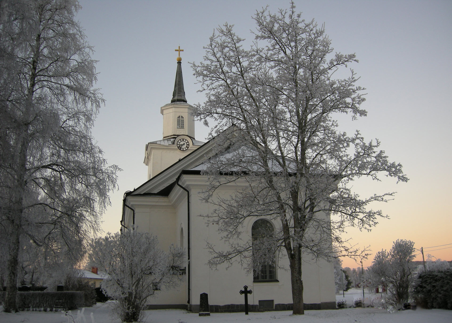 Multrå kyrka i vinterskrud omgiven av frostnupna träd.