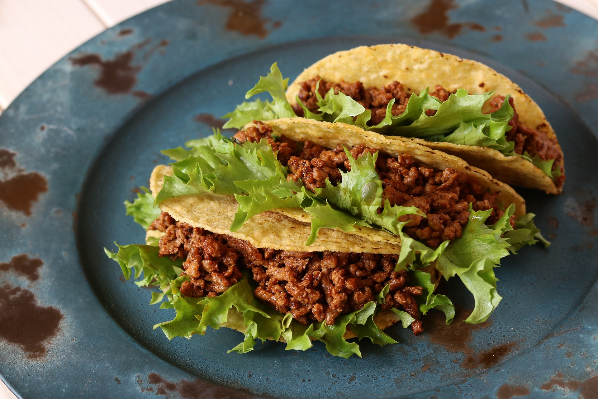 En blå tallrik med tre köttfärsfyllda tacoskal.