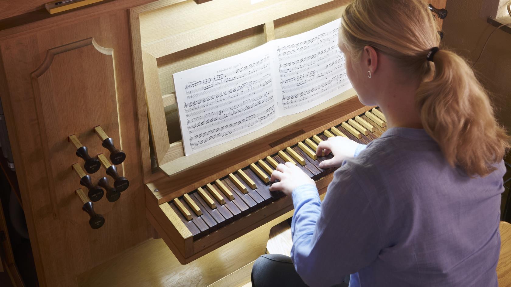 I bild syns ryggen på en kvinnlig organist som spelar orgel.