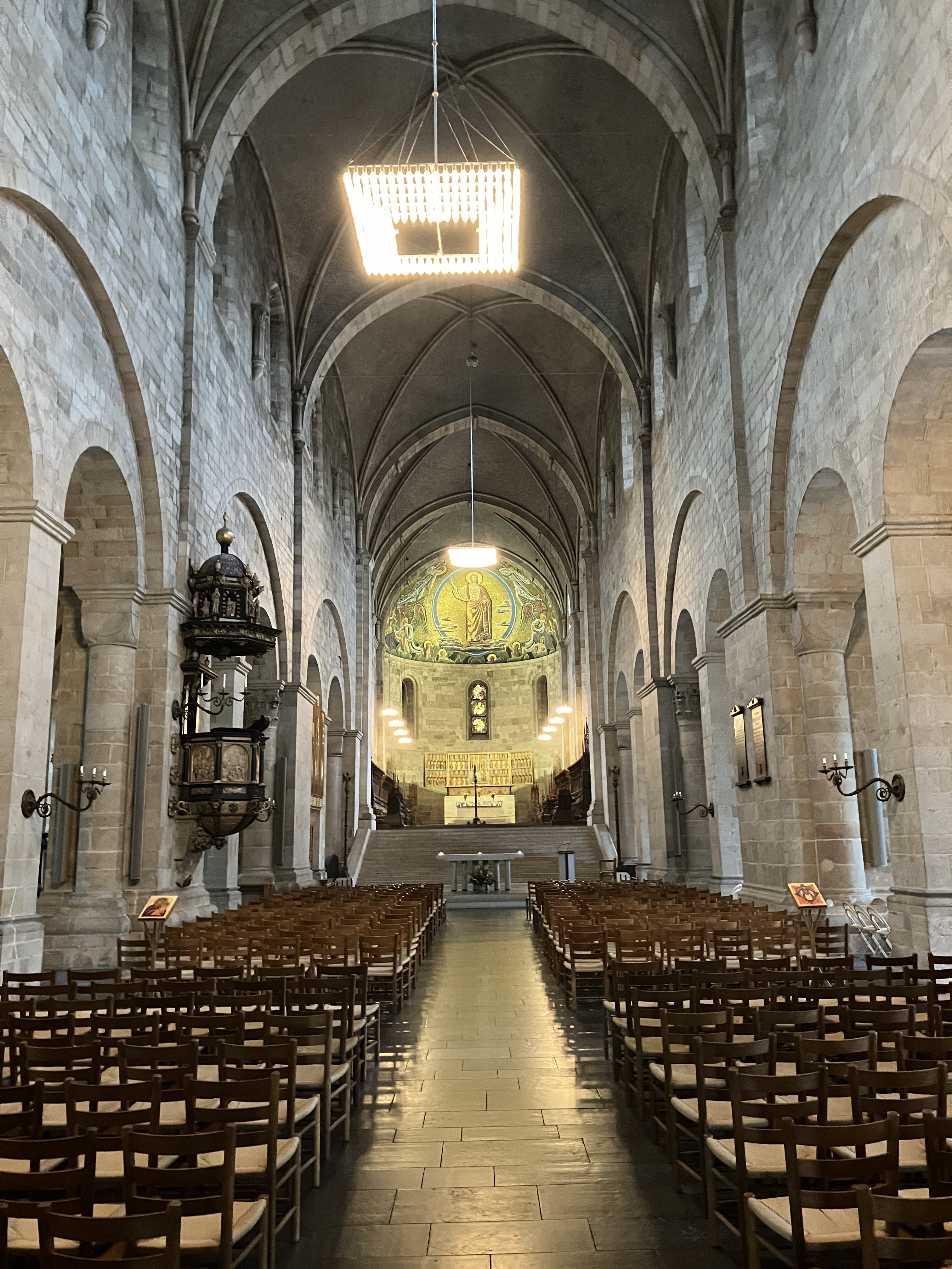 Mittskeppet i Lunds domkyrka med rader av stolar och altare och Kristusmosaik längst frami koret.
