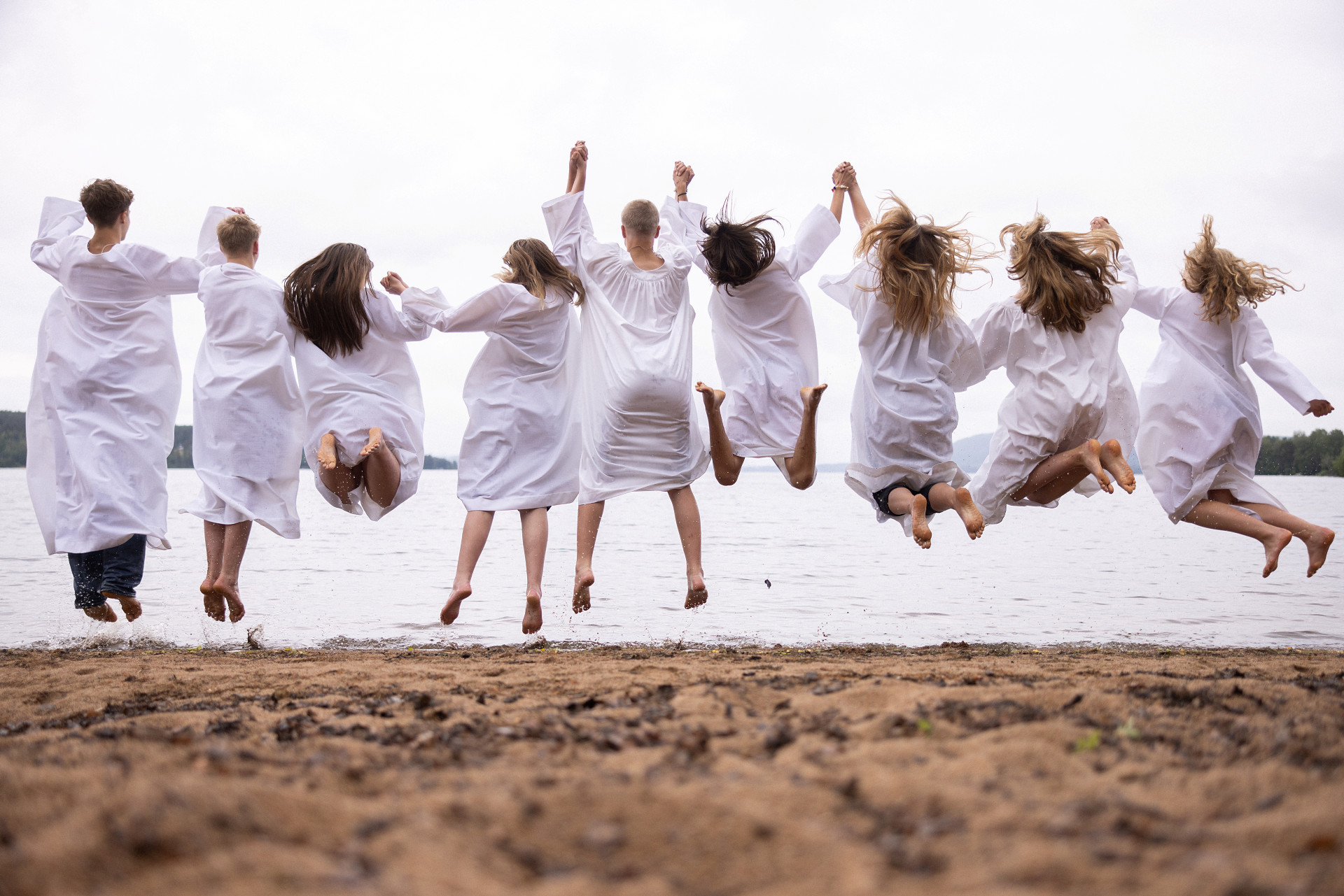 En grupp hoppande konfirmander på en strand, fotade bakifrån