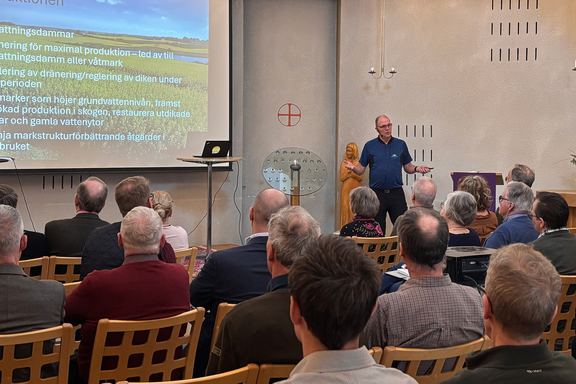 En man föreläser inför publik. På duken syns en powerpointpresentation.