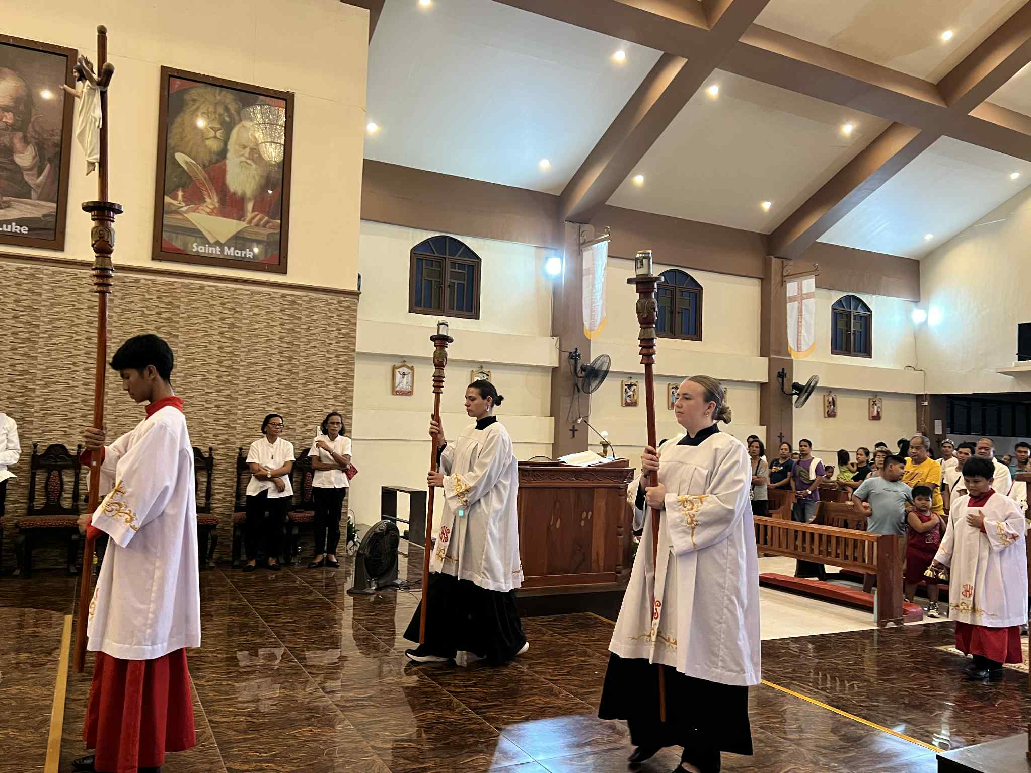 Tre personer klädda i vitt bär kors och ljus fram i en kyrka i Filipinerna.