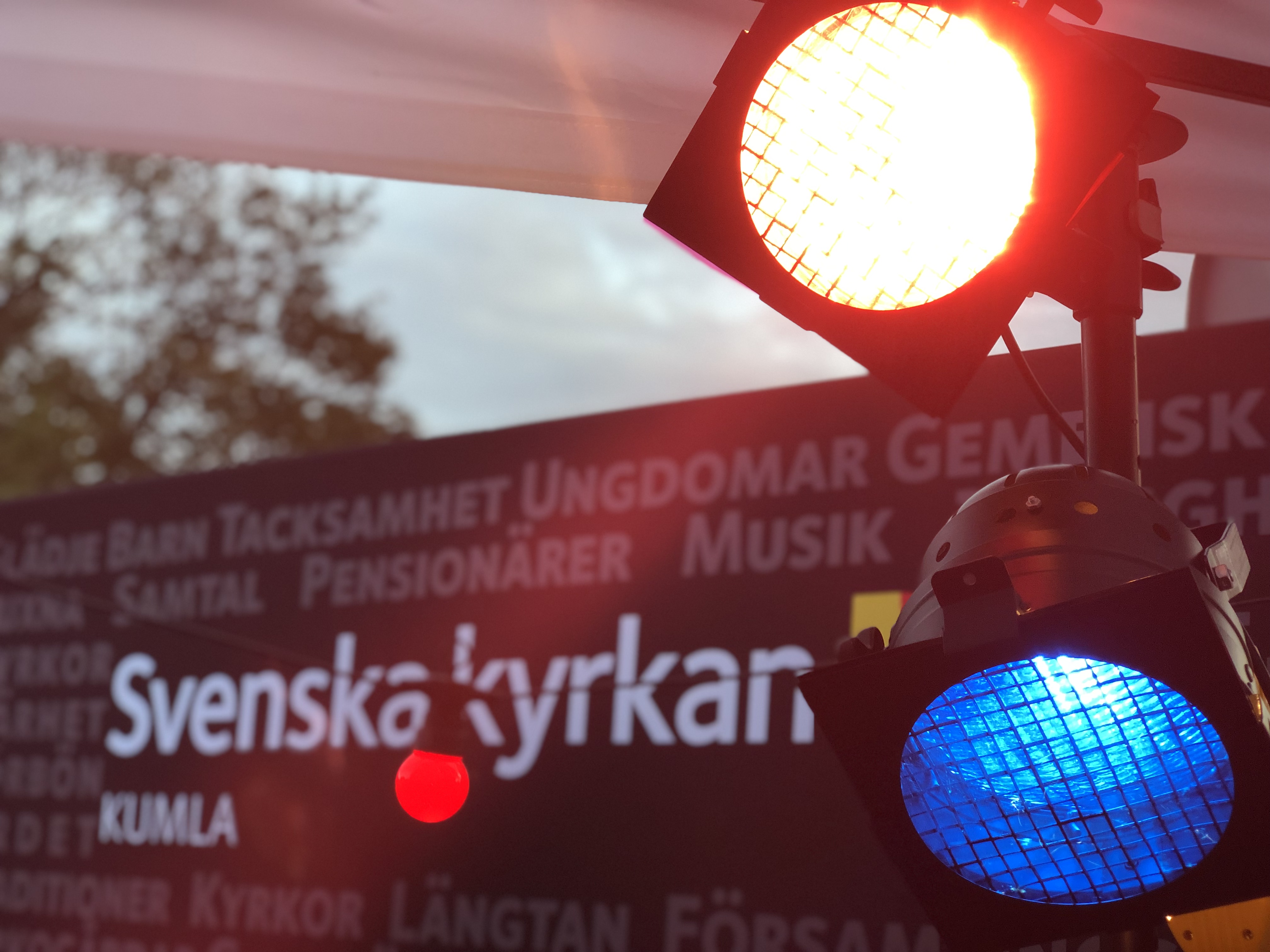 Två strålkastare i förgrunden. Skylt med Svenska kyrkans logotype i bakgrunden