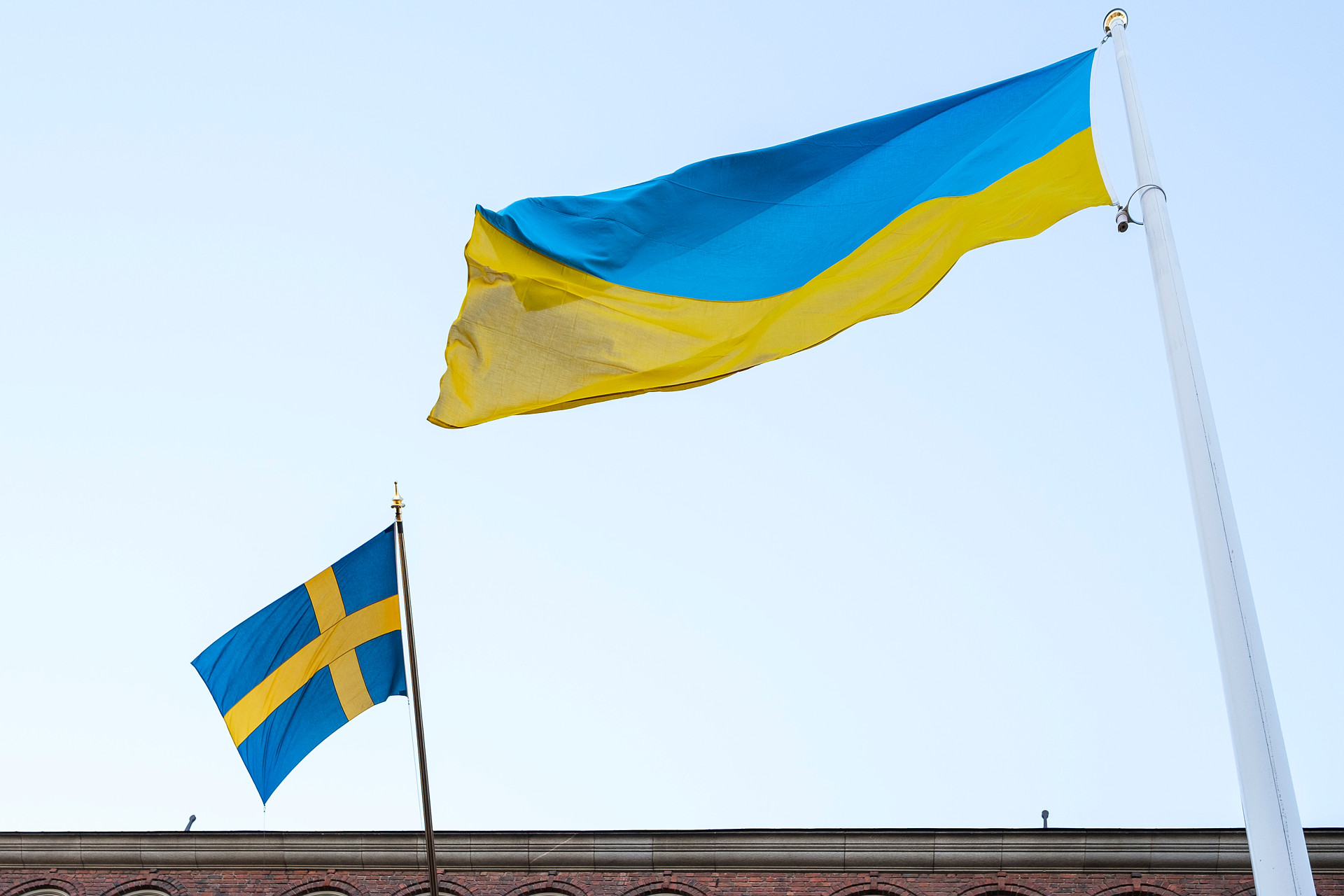 Två blågula flaggor mot ljusblå himmel, en svensk och en ukrainsk.