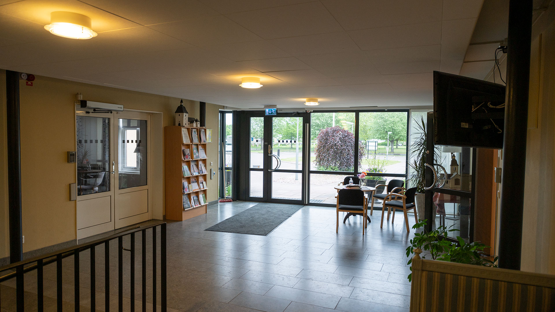 Ett entrérum med glasparti på den sidan där ingången är. Klinkergolvet återspeglar ljuset utifrån. Väggarna är gula och det finns en dörr med glasparti in till Enebysalen på vänster sida. 
