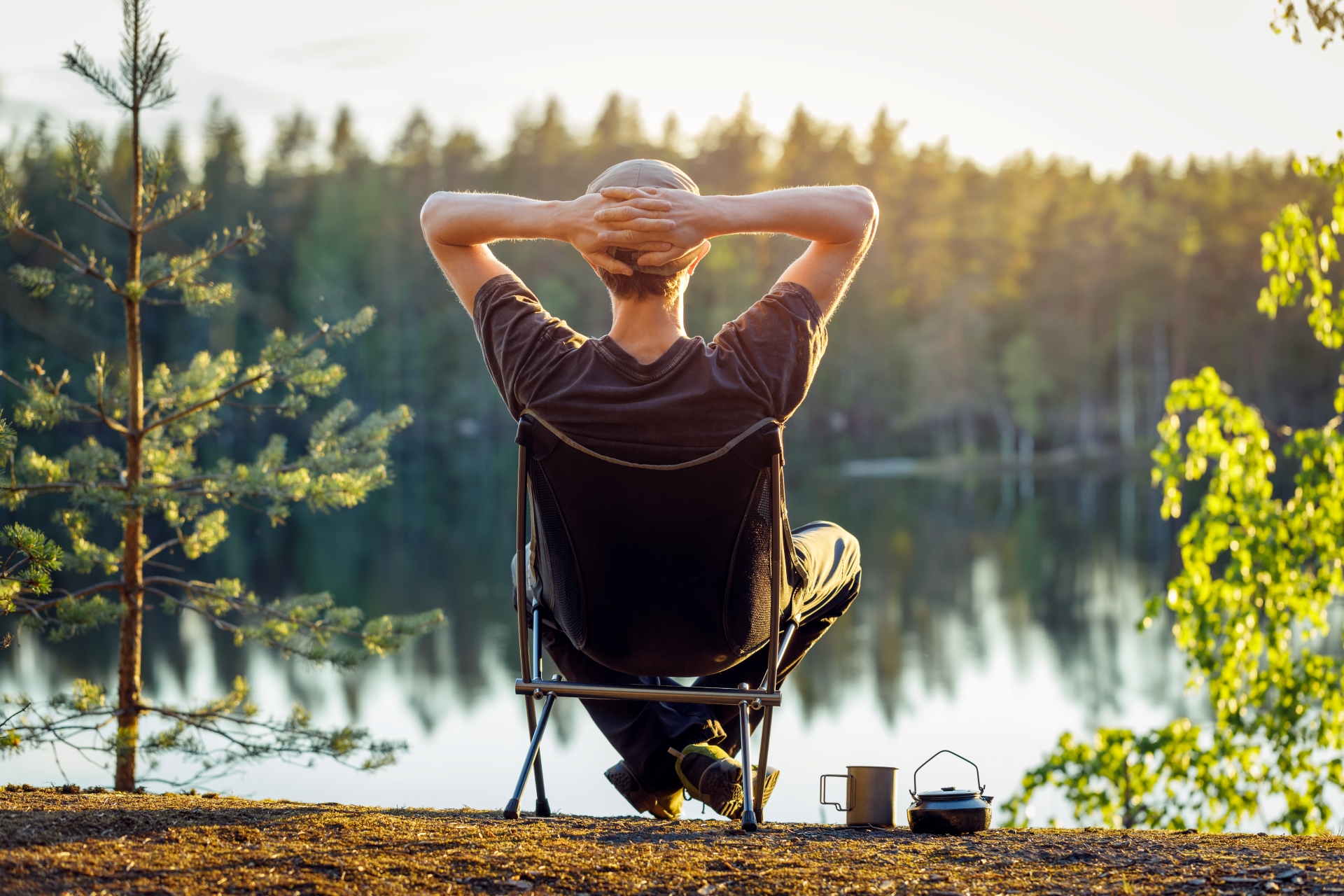 En man sitter på en campingstol vid en skogssjö.