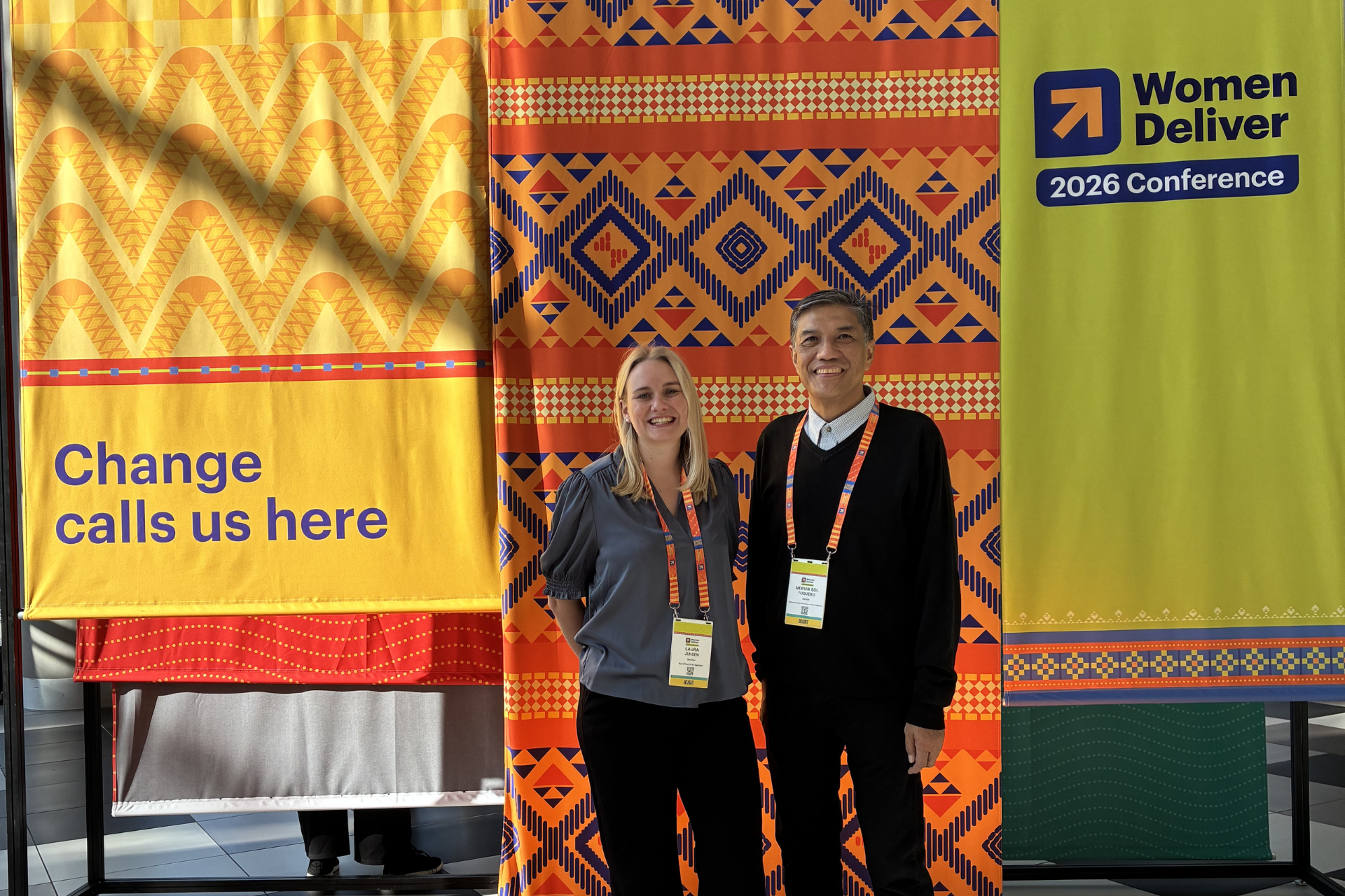 Kvinna och man framför färgglada roll-ups från Women Deliver konferensen i Melbourne 2026.