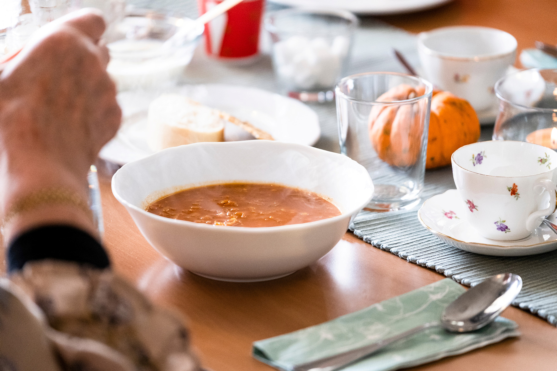 En enkel tallrik med orangebrun rykande soppa. Bordet runt omkring är fyllt av glas, koppar, bröd och dekorationer.