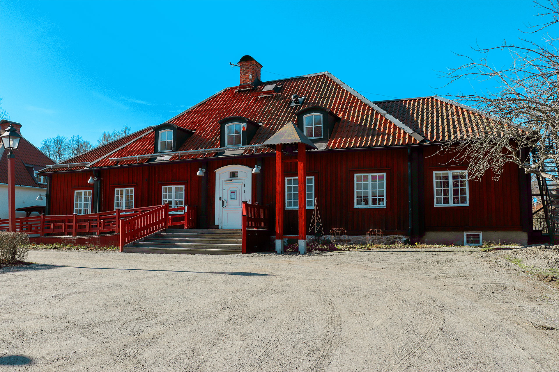En faluröd träbyggnad med orange tegeltak. I bakgrunden en klarblå himmel. 
