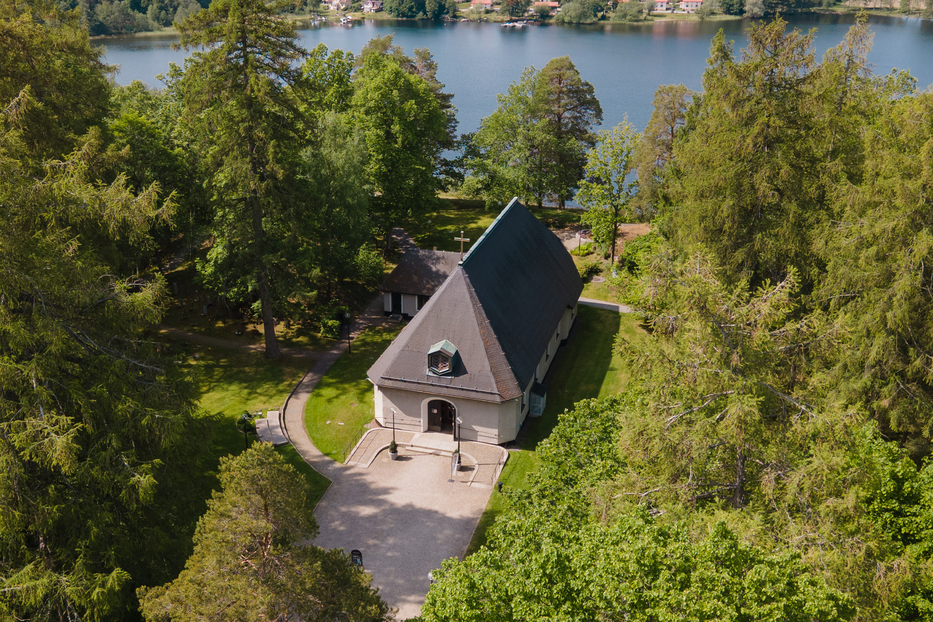 Tullinge kyrka fotograferad från ovan. Runt kyrkan syns grönskande träd och gräs och Tullingesjön