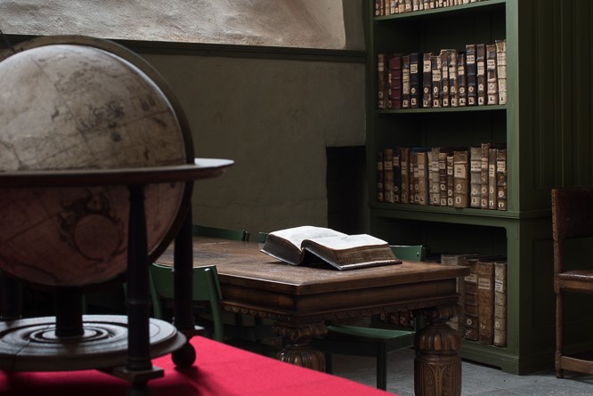En gammal jordglob, en uppslagen bok på ett bord och en bokhylla i Domkyrkobiblioteket.