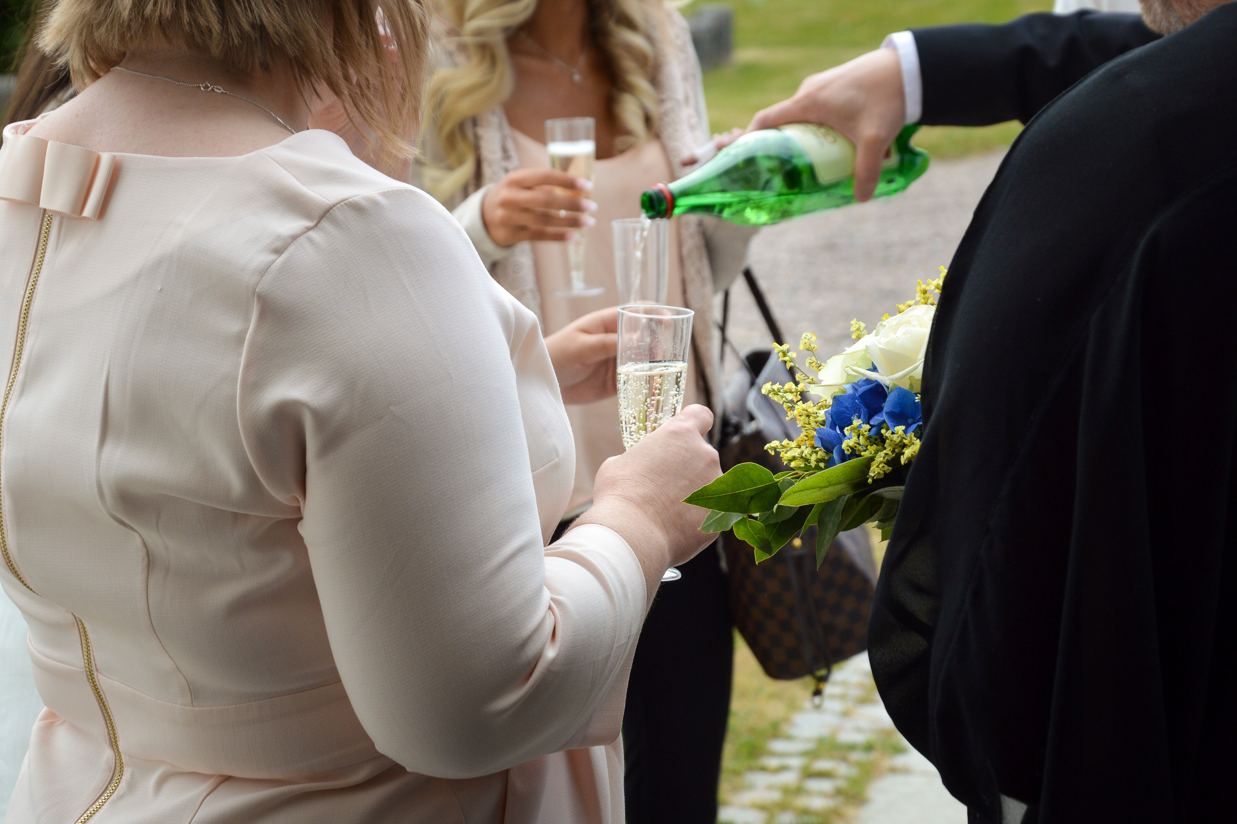 Någon i kostym står utomhus och häller upp cider till några kvinnor.
