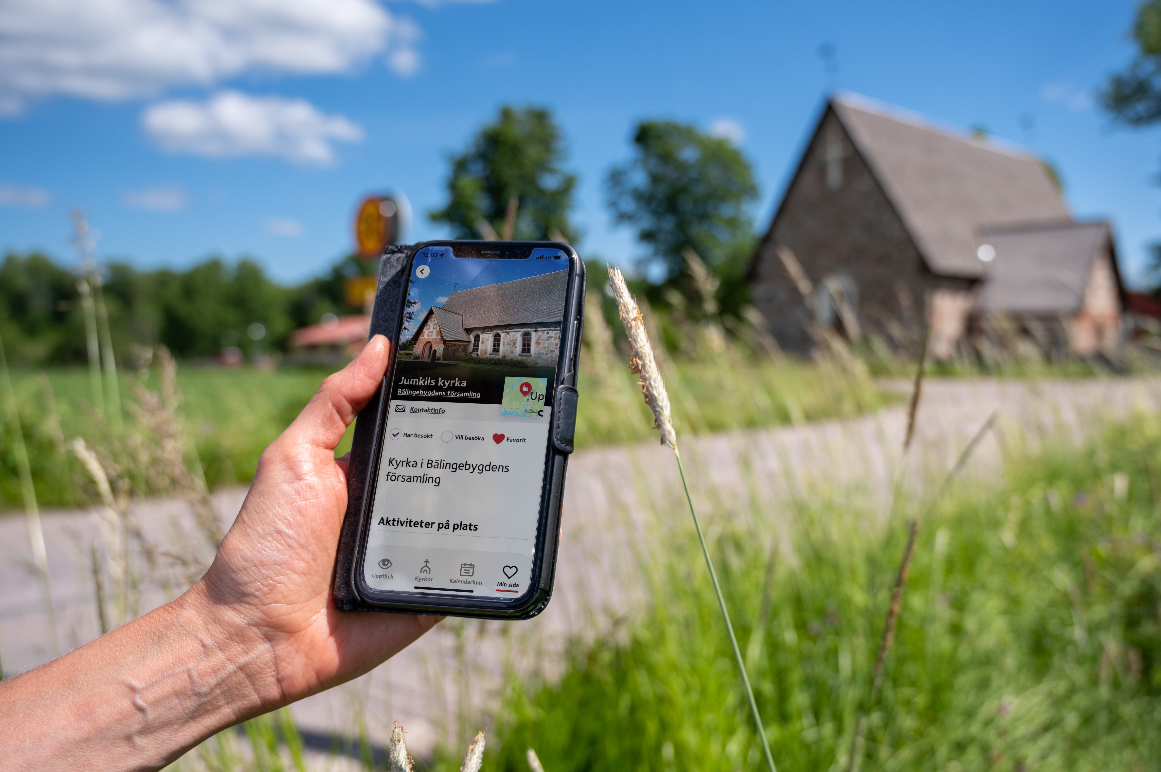 En hand håller i en mobil med skärmbild om kyrkguiden som visar adressen för kyrkan.