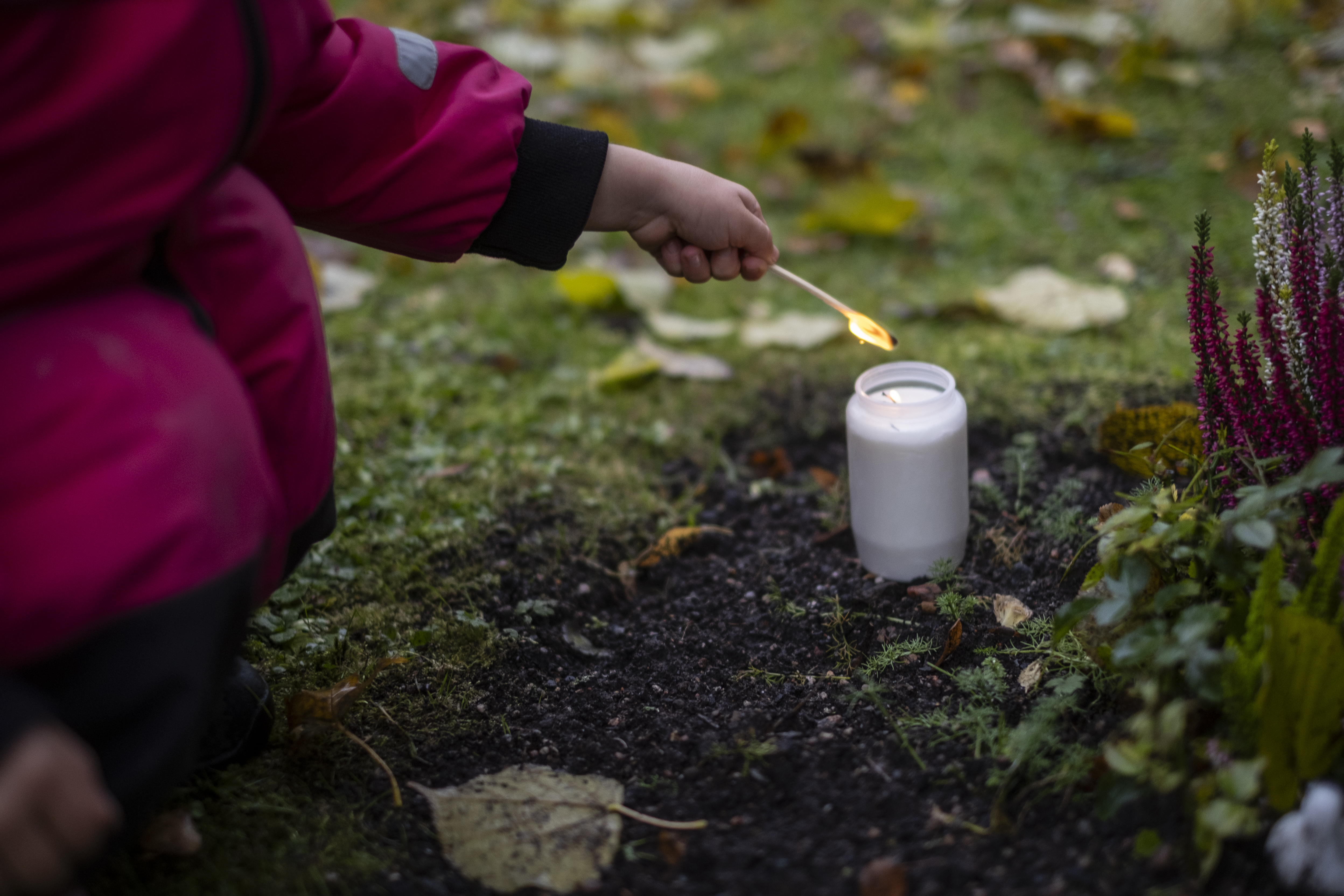 Ett litet barn tänder ett ljus vid en gravsten.