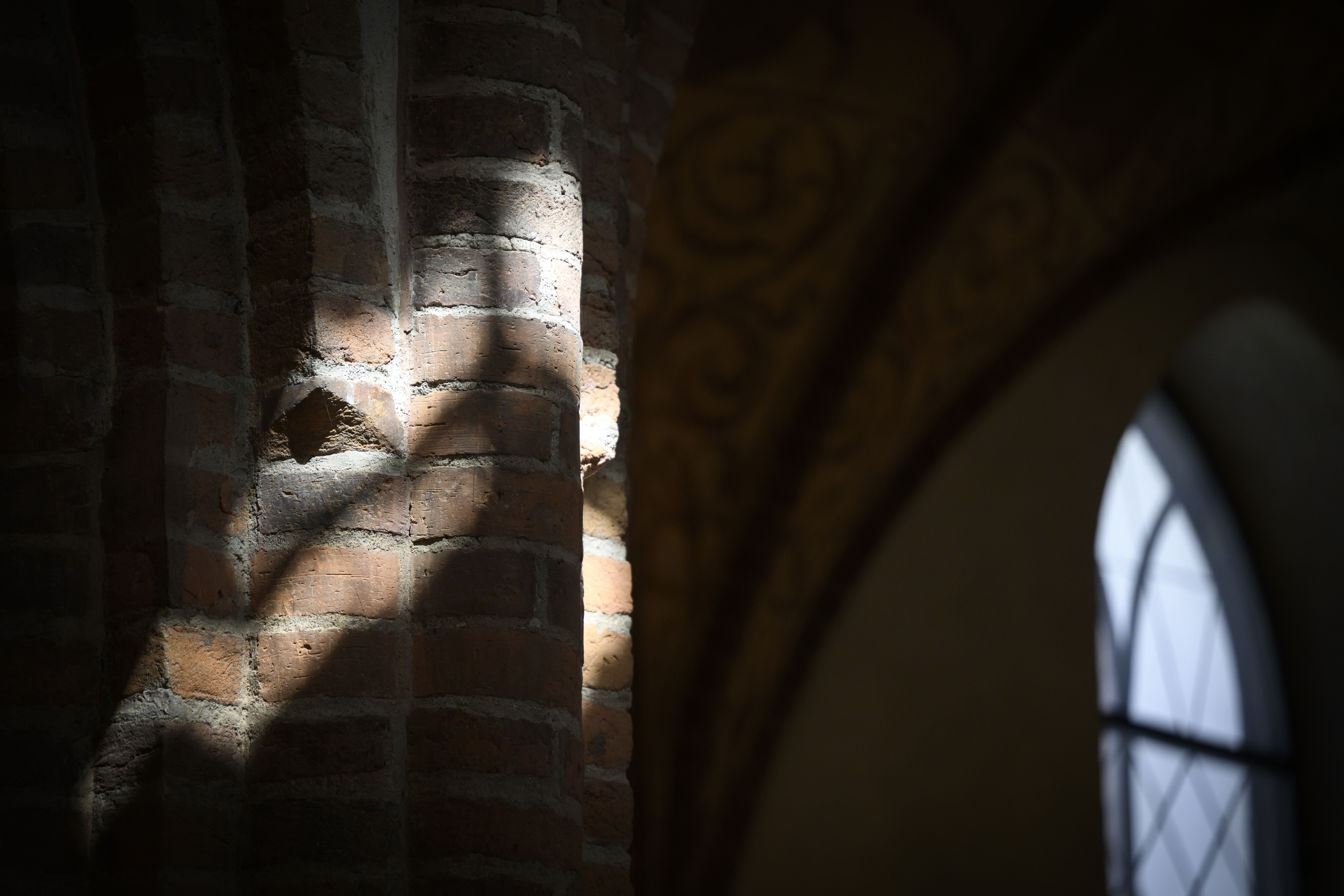Solljuset skiner in på några pelare i rött tegel i en kyrka.