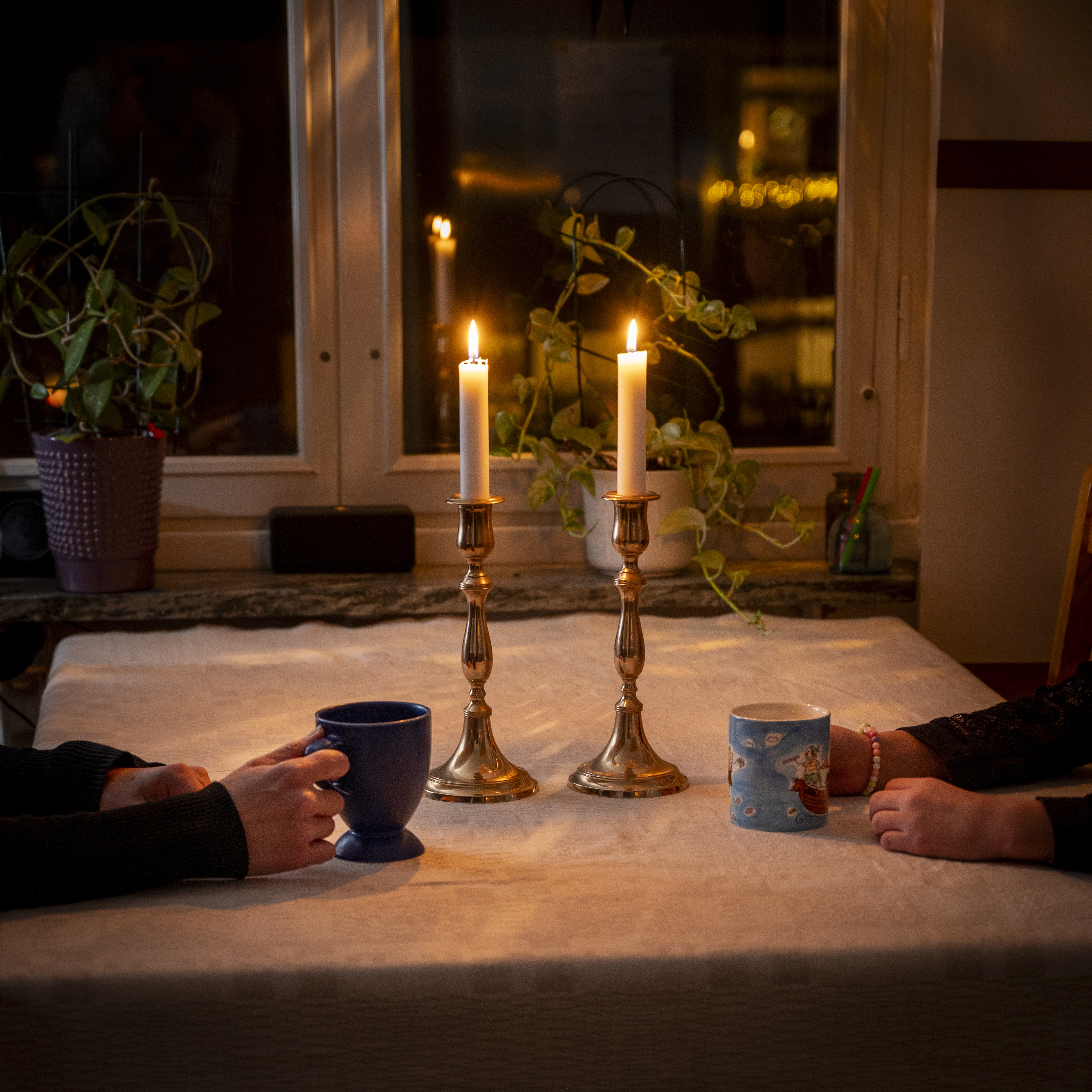 Fika med samtal mellan två personer i hemmamiljö. Levande ljus på bordet.