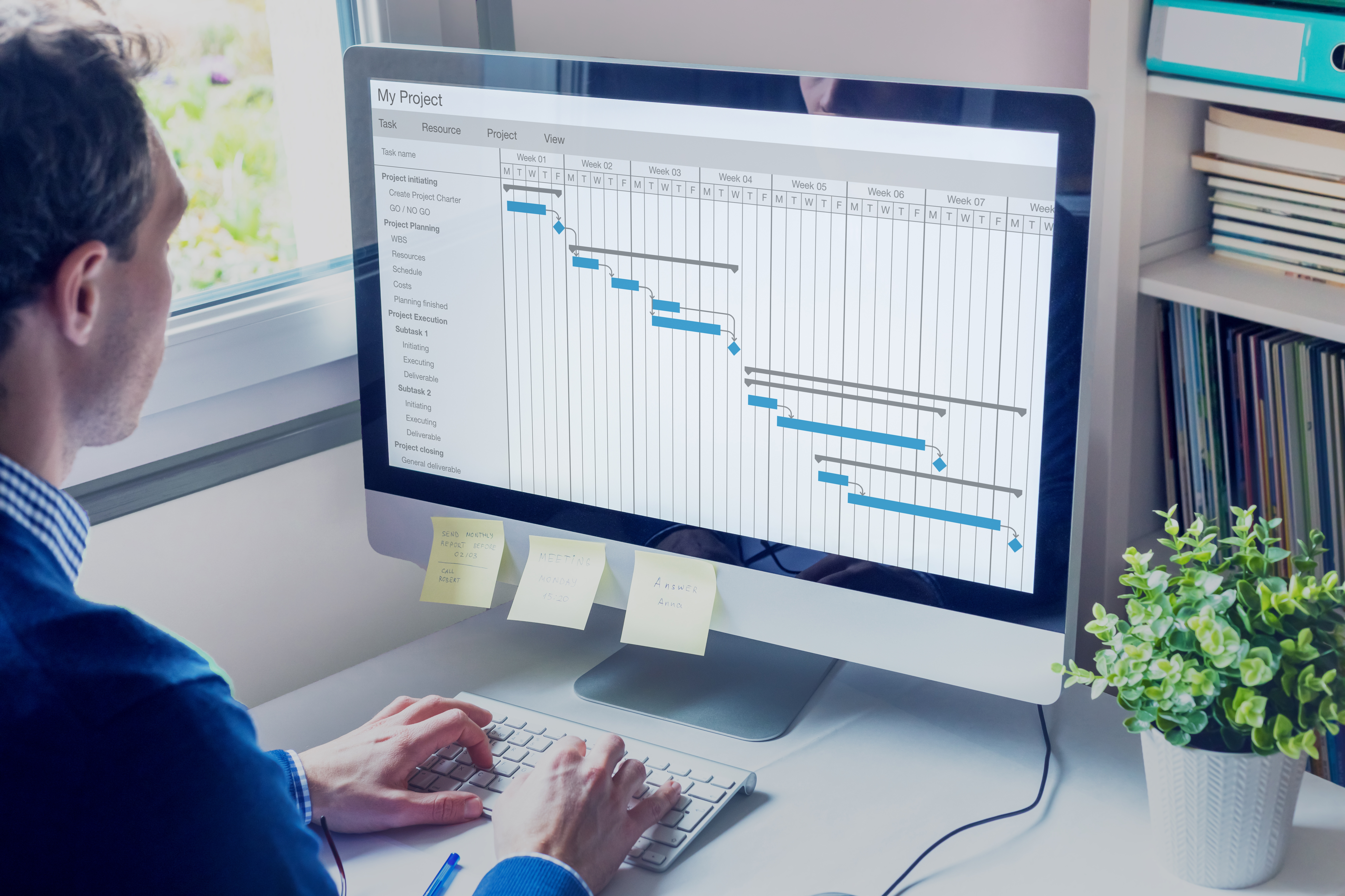 En person sitter vid sin dator. På skärmen syns ett gantt-schema för ett projekt.