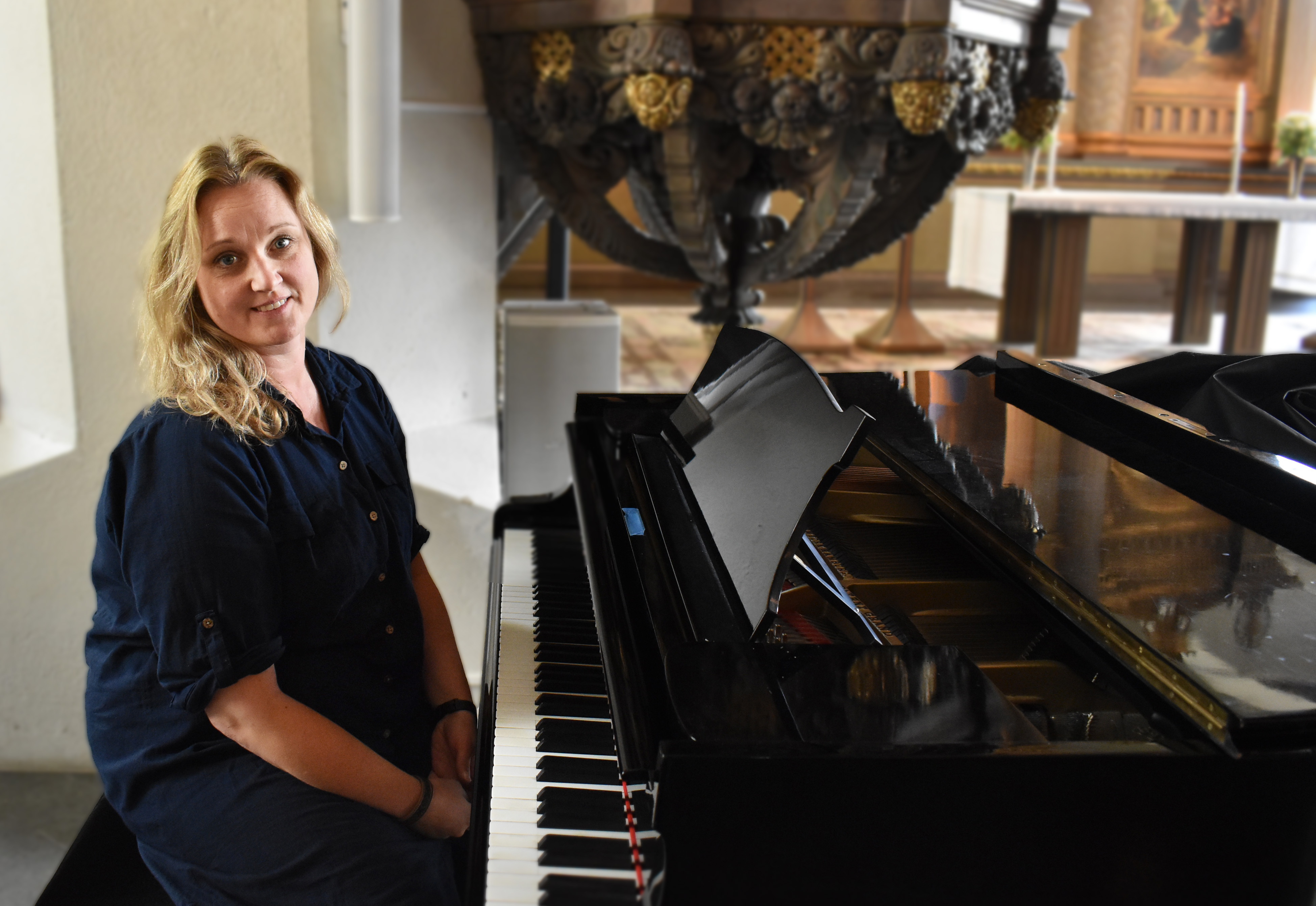 Blond kvinna vid klaviatur i kyrka.